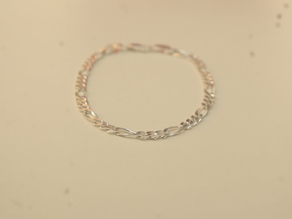 The silver figaro chain bracelet laid in a circle.
