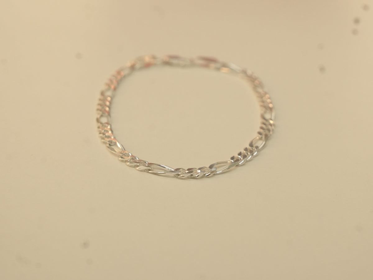 The silver figaro chain bracelet laid in a circle.