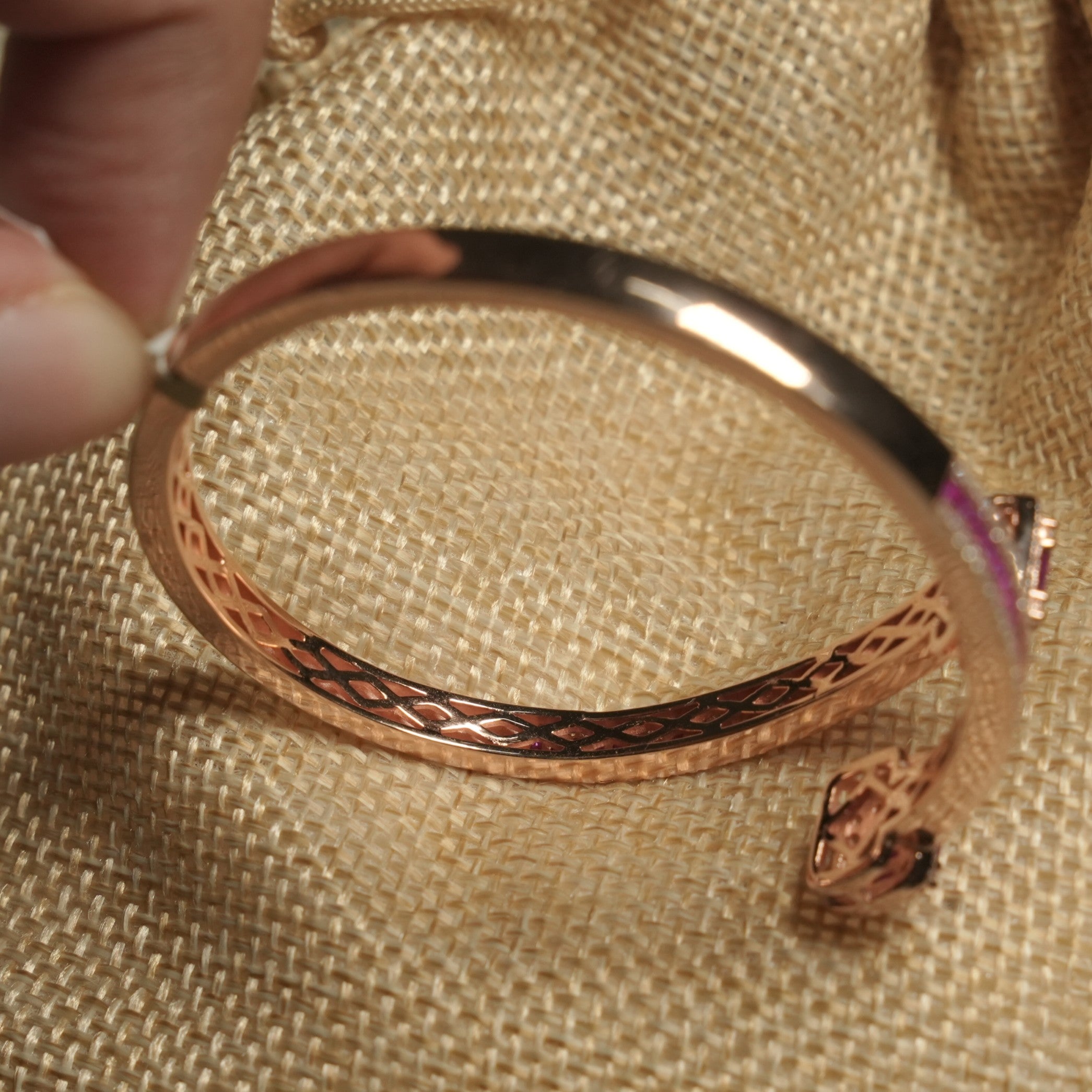 Side view of the bangle held in hand, showing its lattice-pierced inner band and polished rose gold-tone finish.