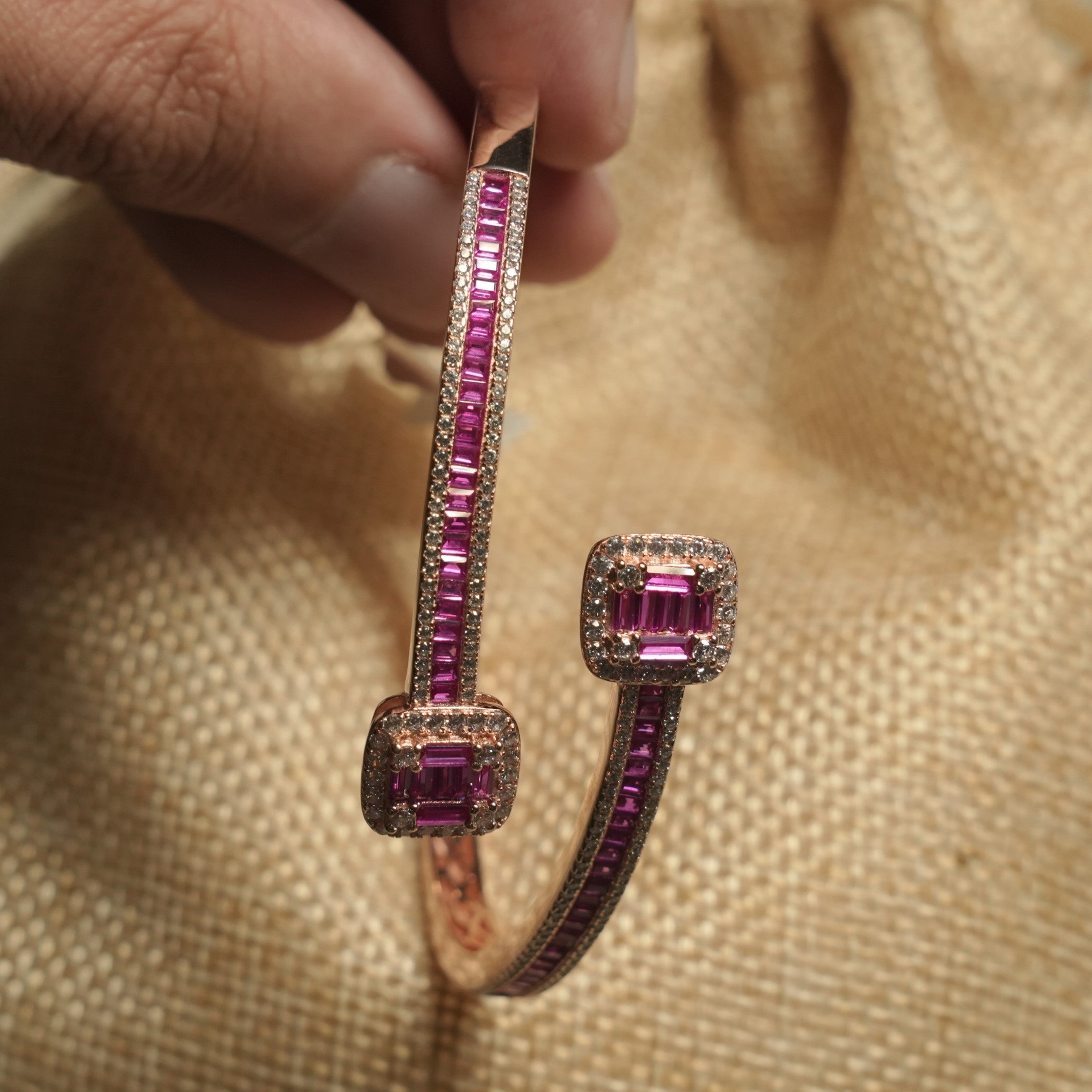 Hand holding the open bypass bangle upright, showing the magenta baguette rows and cushion-shaped halo tips.