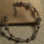Multi-strand textured silver bracelet stationed with fluted silver beads and hammered rose gold-tone beads, with extender chain, resting on a jute pouch.