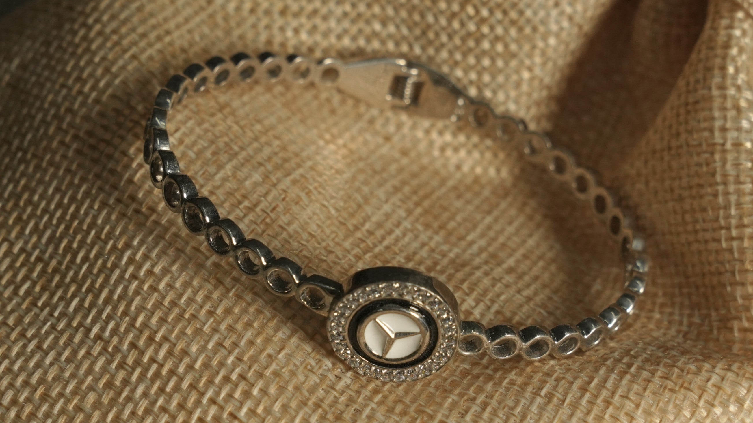 Angled view of the bracelet on a jute pouch, showing the polished open-circle band, hinge and star medallion.