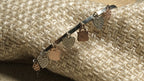 Detail of the bangle's dangling charms, including Bejewelled hearts and rose gold-tone drops, against woven fabric.