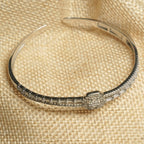 Sterling silver hinged bangle with a channel of baguette cubic zirconia, micro-Bejewelled borders and a square halo centre, resting on a jute pouch.