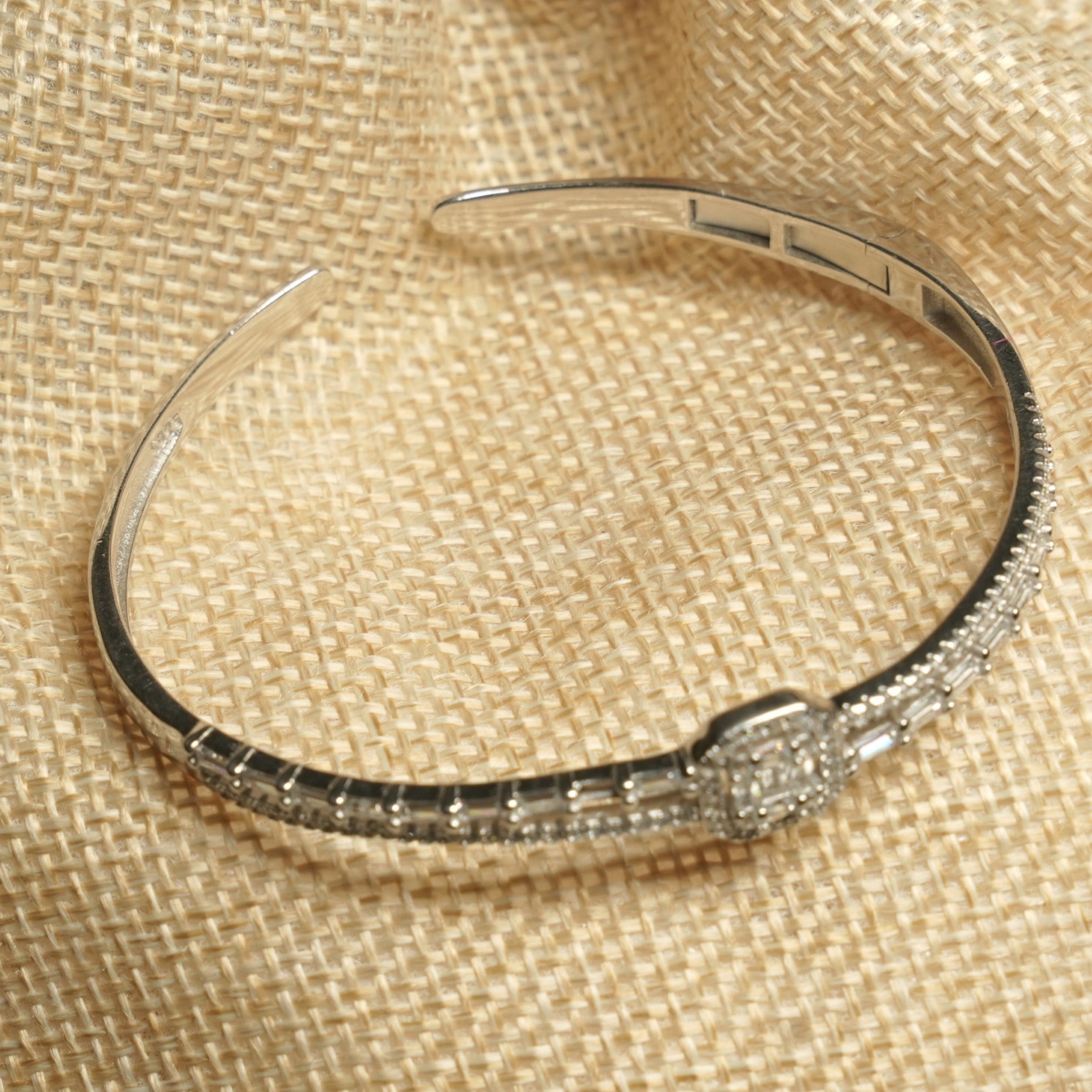 Angled view of the bangle on a jute pouch, showing the polished plain half of the band and the set half meeting at the halo centre.