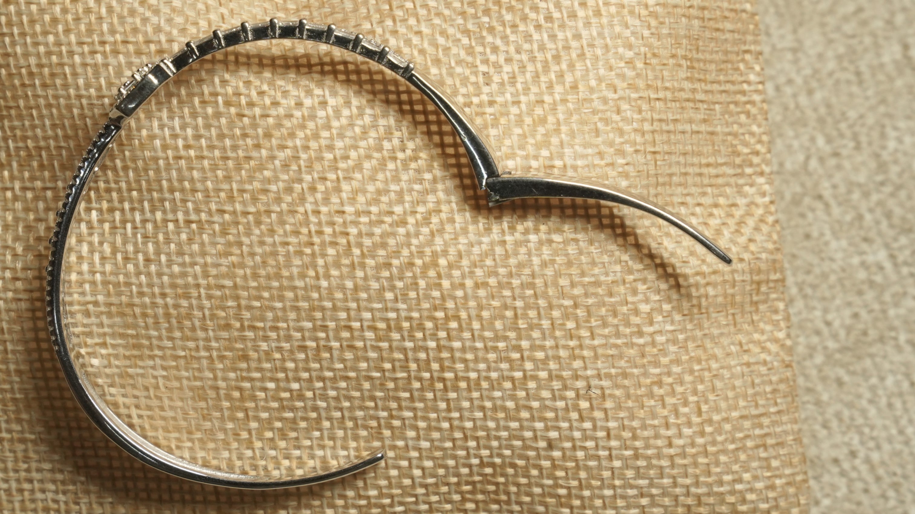 The bangle shown fully open on its hinge against jute fabric, revealing the smooth inner band.