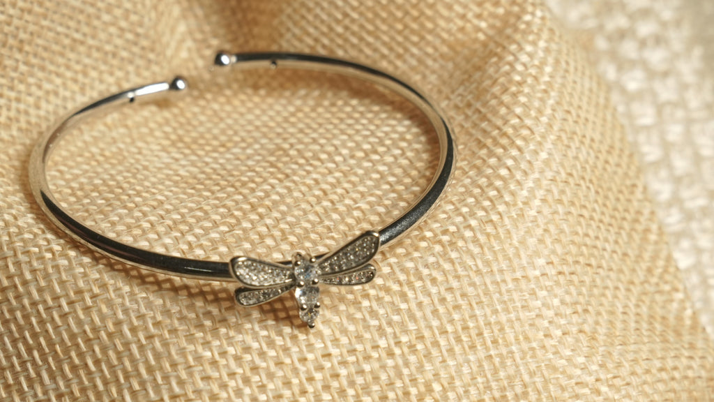 The dragonfly cuff resting on a jute pouch, showing Bejewelled wings and a body set with marquise and round cubic zirconia.