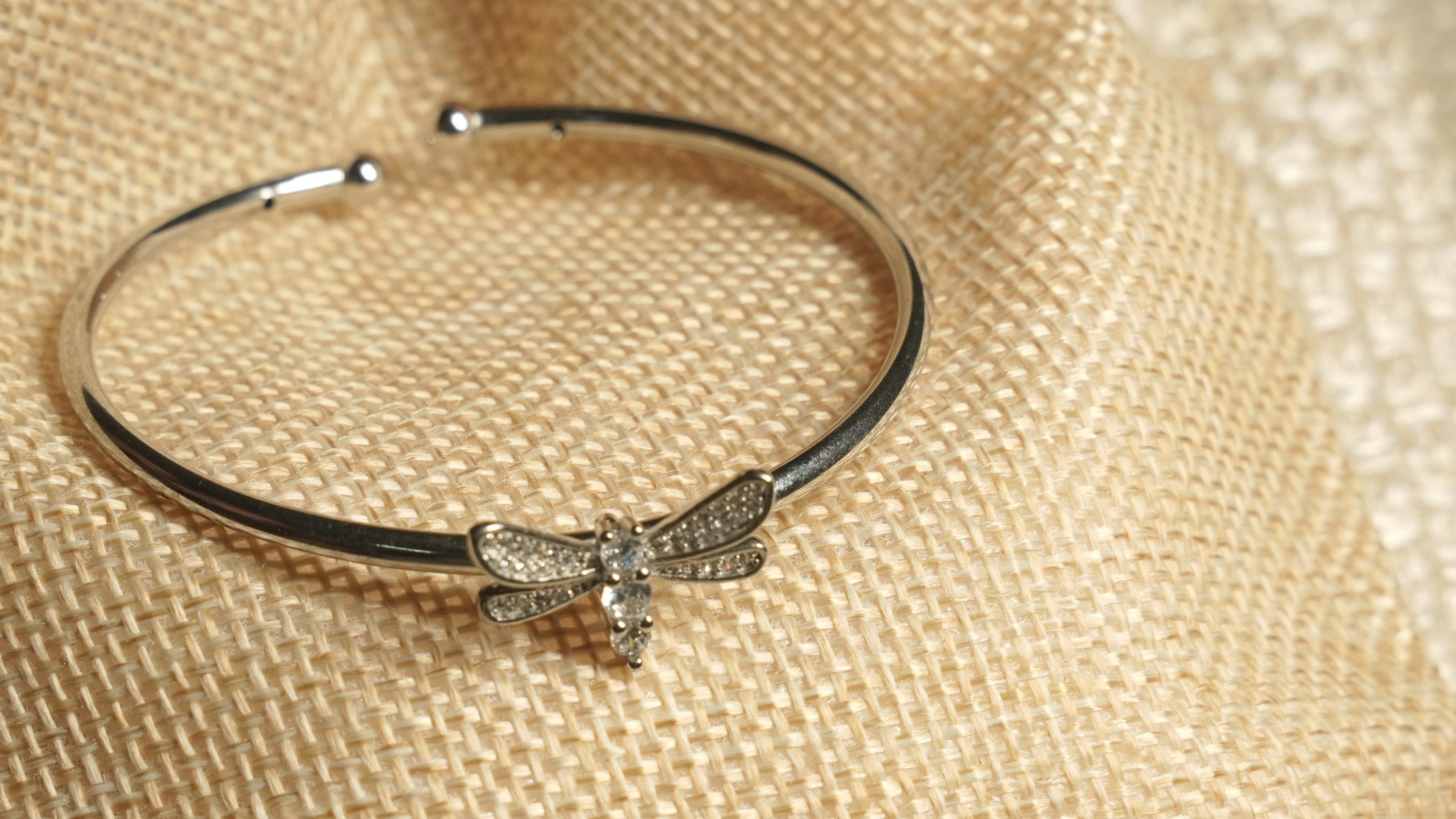 The dragonfly cuff resting on a jute pouch, showing Bejewelled wings and a body set with marquise and round cubic zirconia.