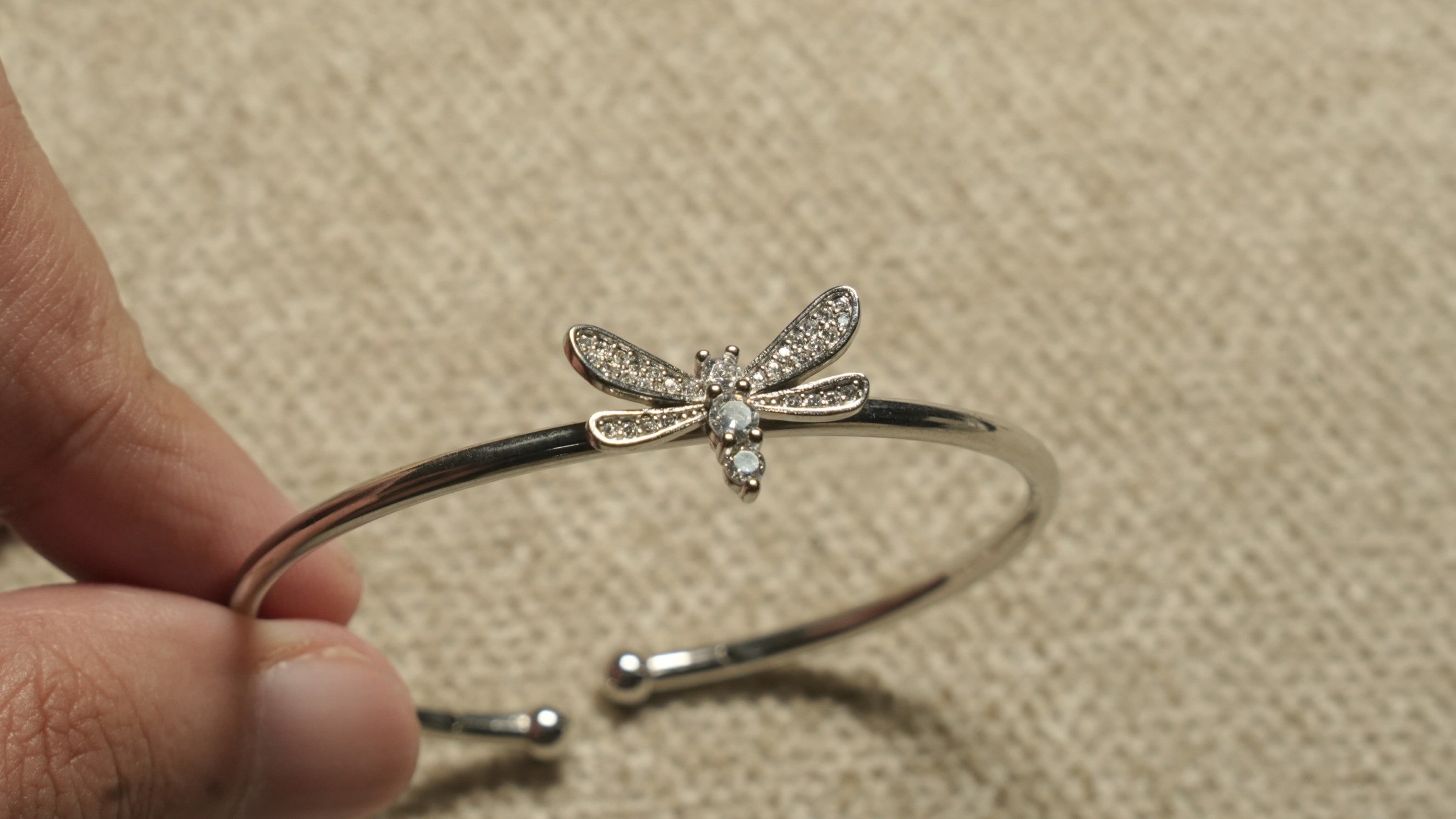 Hand holding the open cuff, showing the dragonfly motif and the rounded ball terminals at the opening.