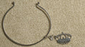 Slim sterling silver wire cuff with ball ends and a dangling openwork crown charm, laid on beige fabric.