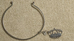Slim sterling silver wire cuff with ball ends and a dangling openwork crown charm, laid on beige fabric.