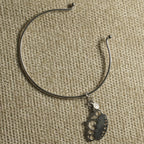 The wire cuff turned on woven fabric, showing the pierced crown charm and small round tag on its link.