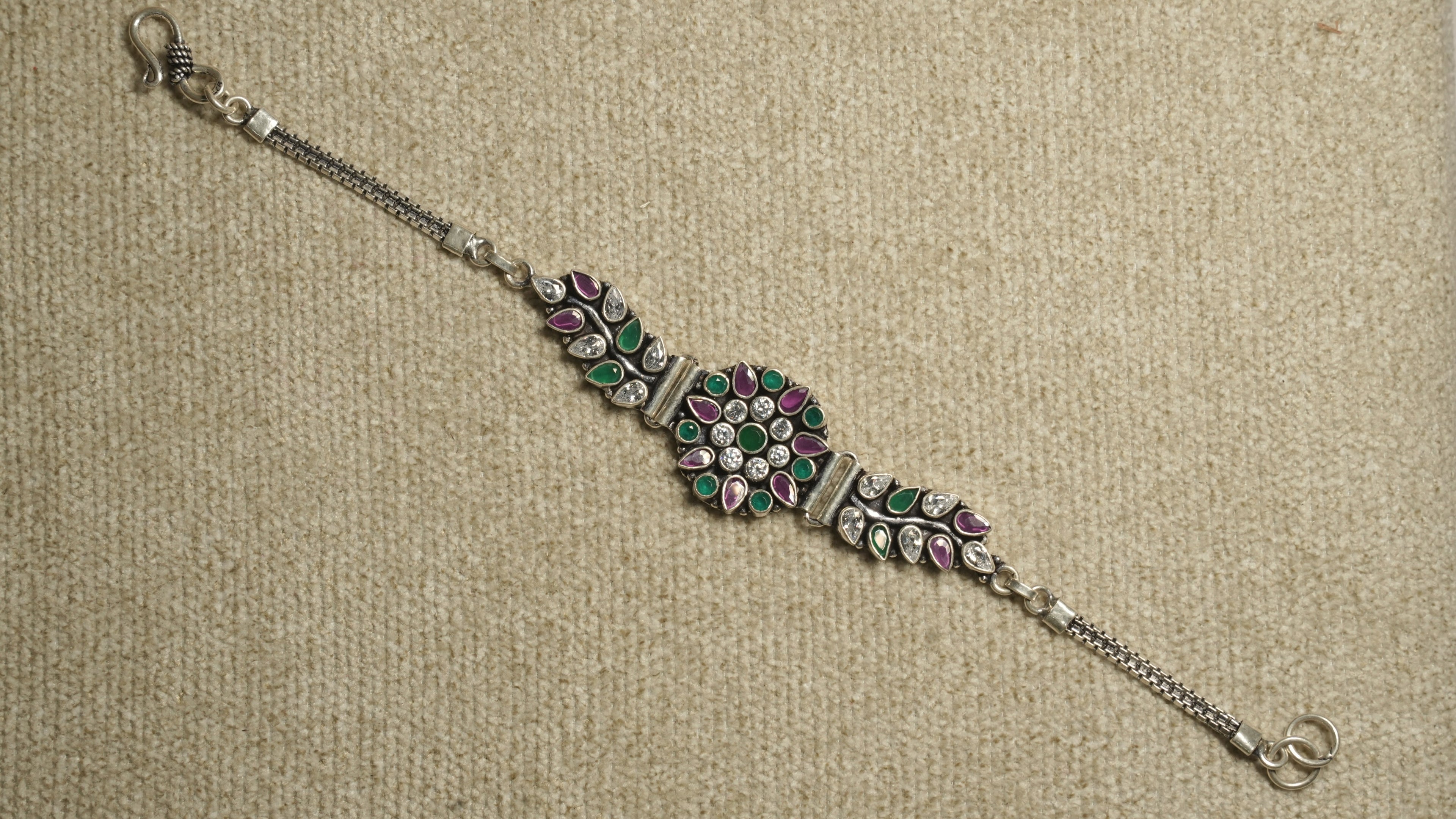Oxidised sterling silver bracelet with a round floral cluster of white cubic zirconia and green and pink stones, leaf-set side panels, box chaiMG and an S-hook clasp.