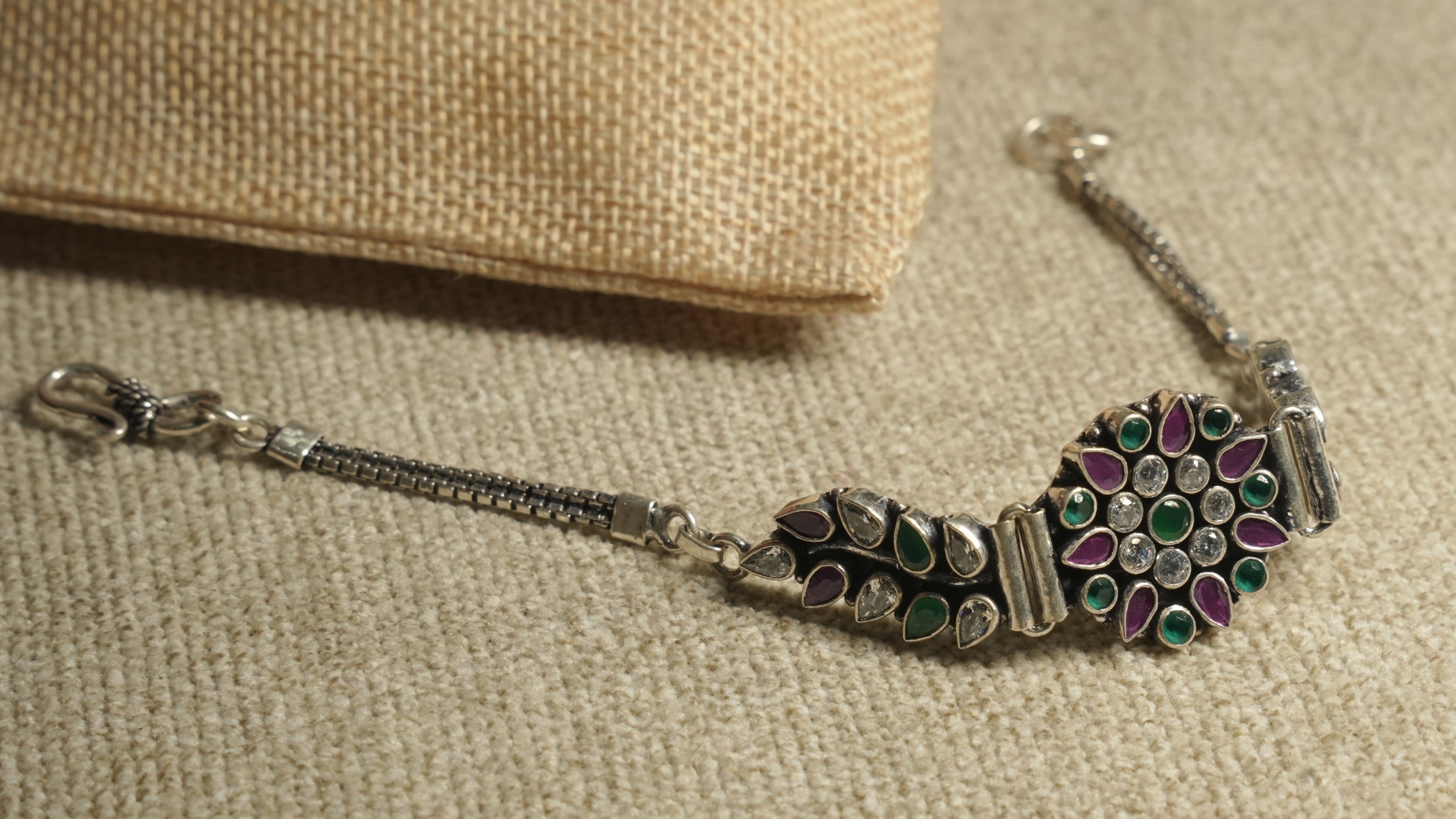 The floral panel bracelet resting on beige fabric, showing its green and pink teardrop stones around the white cubic zirconia rosette.