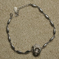 Sterling silver bracelet of marquise-shaped links centred on an open circle with a Bejewelled crown and a suspended cubic zirconia, laid flat on beige fabric.
