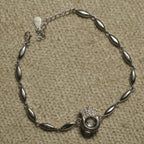 Sterling silver bracelet of marquise-shaped links centred on an open circle with a Bejewelled crown and a suspended cubic zirconia, laid flat on beige fabric.