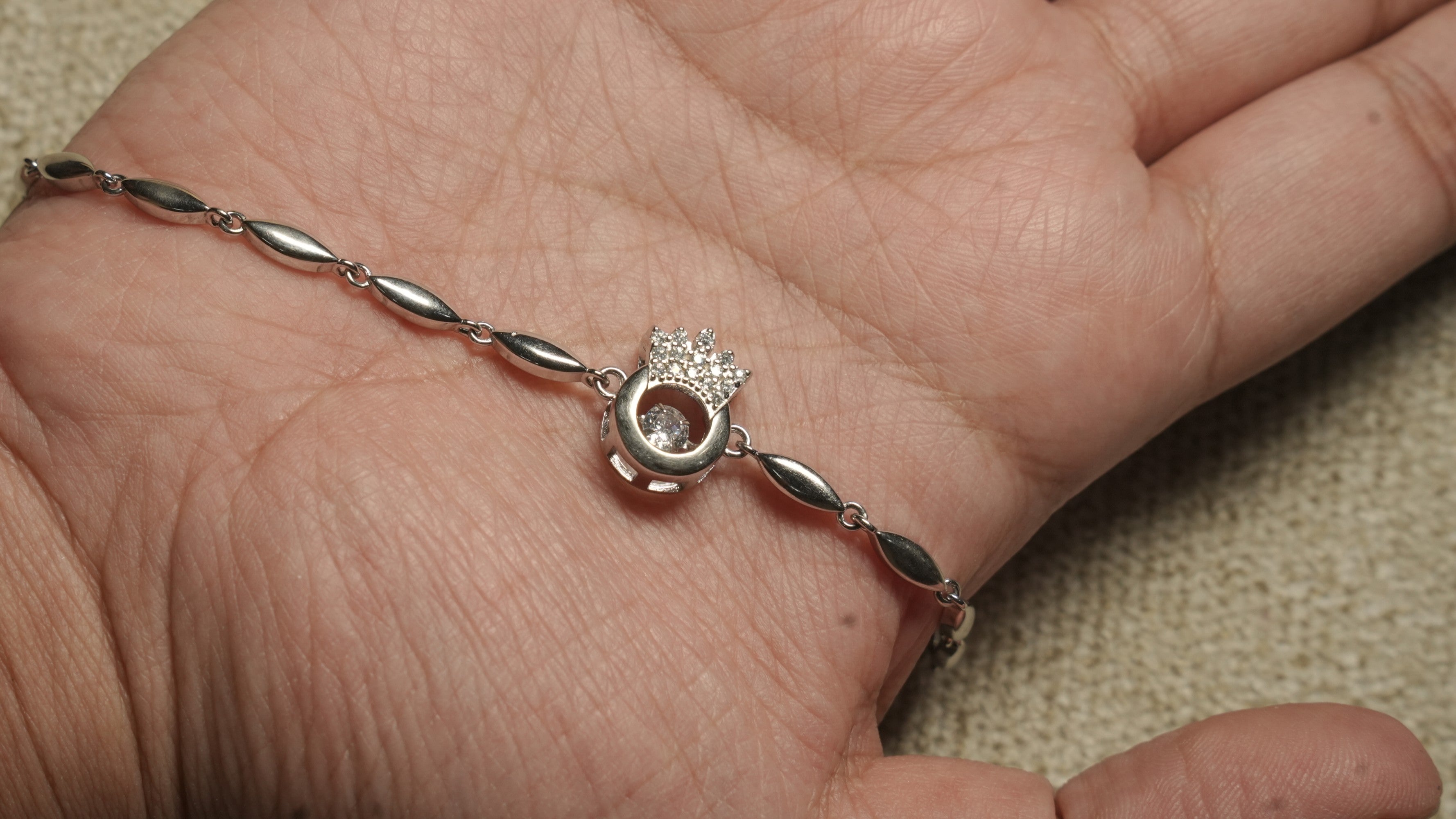 The bracelet draped across an open palm, showing the crown centrepiece and polished marquise links.