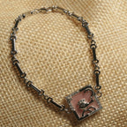 Sterling silver bar-link bracelet with a square pearlescent pink panel framed in cubic zirconia and centred with a fish motif, resting on a jute pouch.