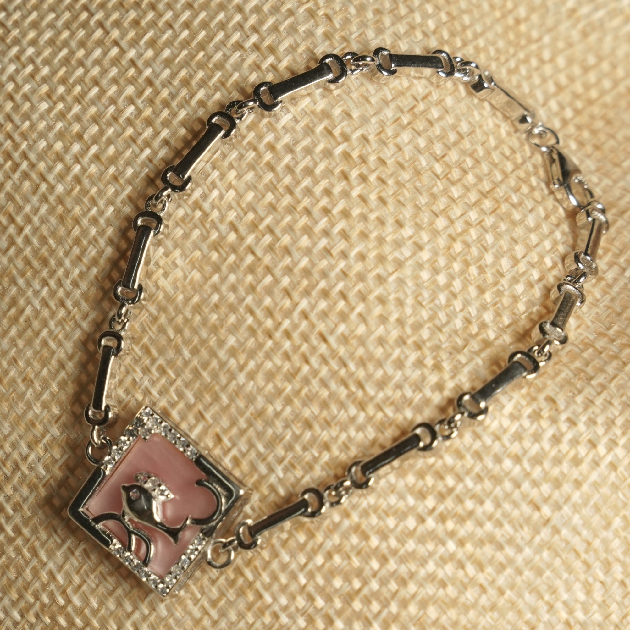 The bracelet angled on woven fabric, showing the fish panel set on point with its cubic zirconia frame and lobster clasp.