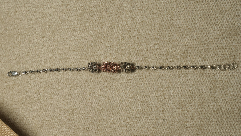 Slim sterling silver bracelet of faceted beads with three fluted bead clusters, the centre one rose gold-tone, laid out straight on beige fabric.