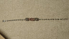 Slim sterling silver bracelet of faceted beads with three fluted bead clusters, the centre one rose gold-tone, laid out straight on beige fabric.