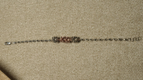 Slim sterling silver bracelet of faceted beads with three fluted bead clusters, the centre one rose gold-tone, laid out straight on beige fabric.