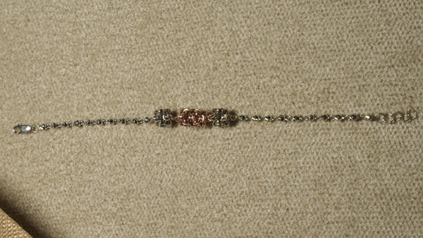 Slim sterling silver bracelet of faceted beads with three fluted bead clusters, the centre one rose gold-tone, laid out straight on beige fabric.