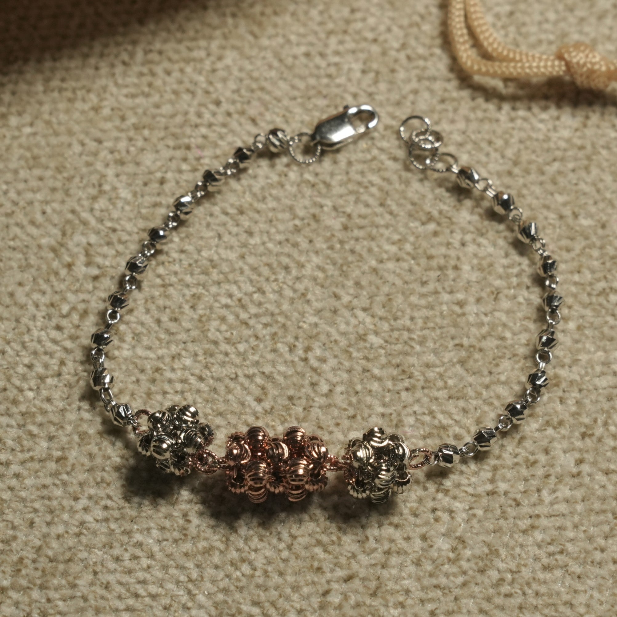 The two-tone bead cluster bracelet arranged in a circle, showing its lobster clasp and extender chain beside a jute pouch.
