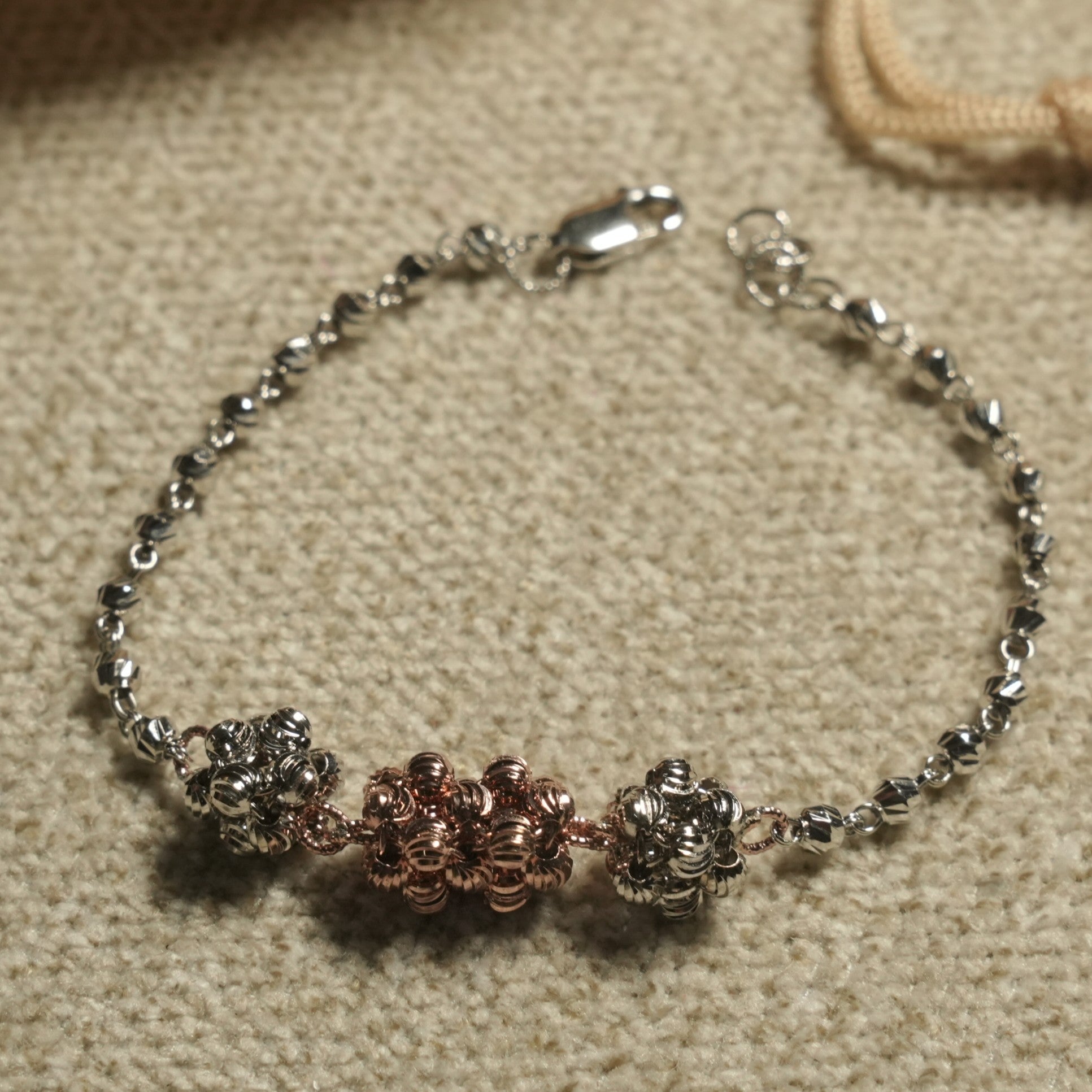 Overhead view of the bracelet showing the rose gold-tone centre cluster flanked by textured silver clusters on a fine beaded chain.