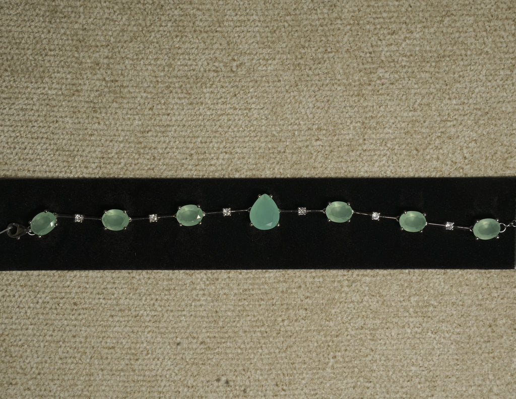 Sterling silver bracelet of prong-set sea-green oval stones with a pear-shaped centre stone, spaced by round cubic zirconia, displayed on black velvet.