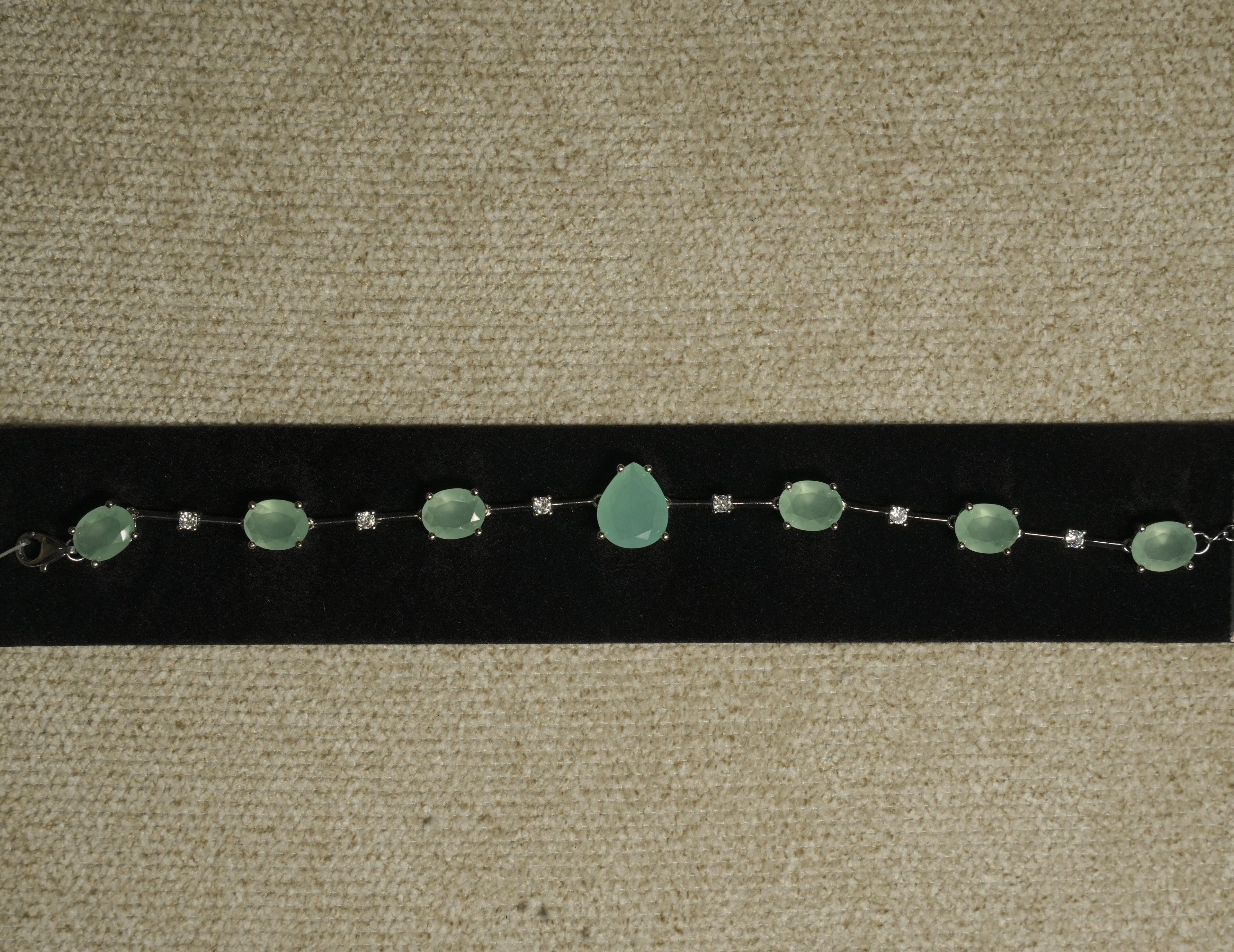 Sterling silver bracelet of prong-set sea-green oval stones with a pear-shaped centre stone, spaced by round cubic zirconia, displayed on black velvet.