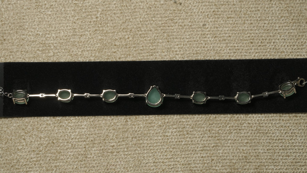 Reverse of the green stone bracelet showing its prong settings, slim bar links and lobster clasp on black velvet.