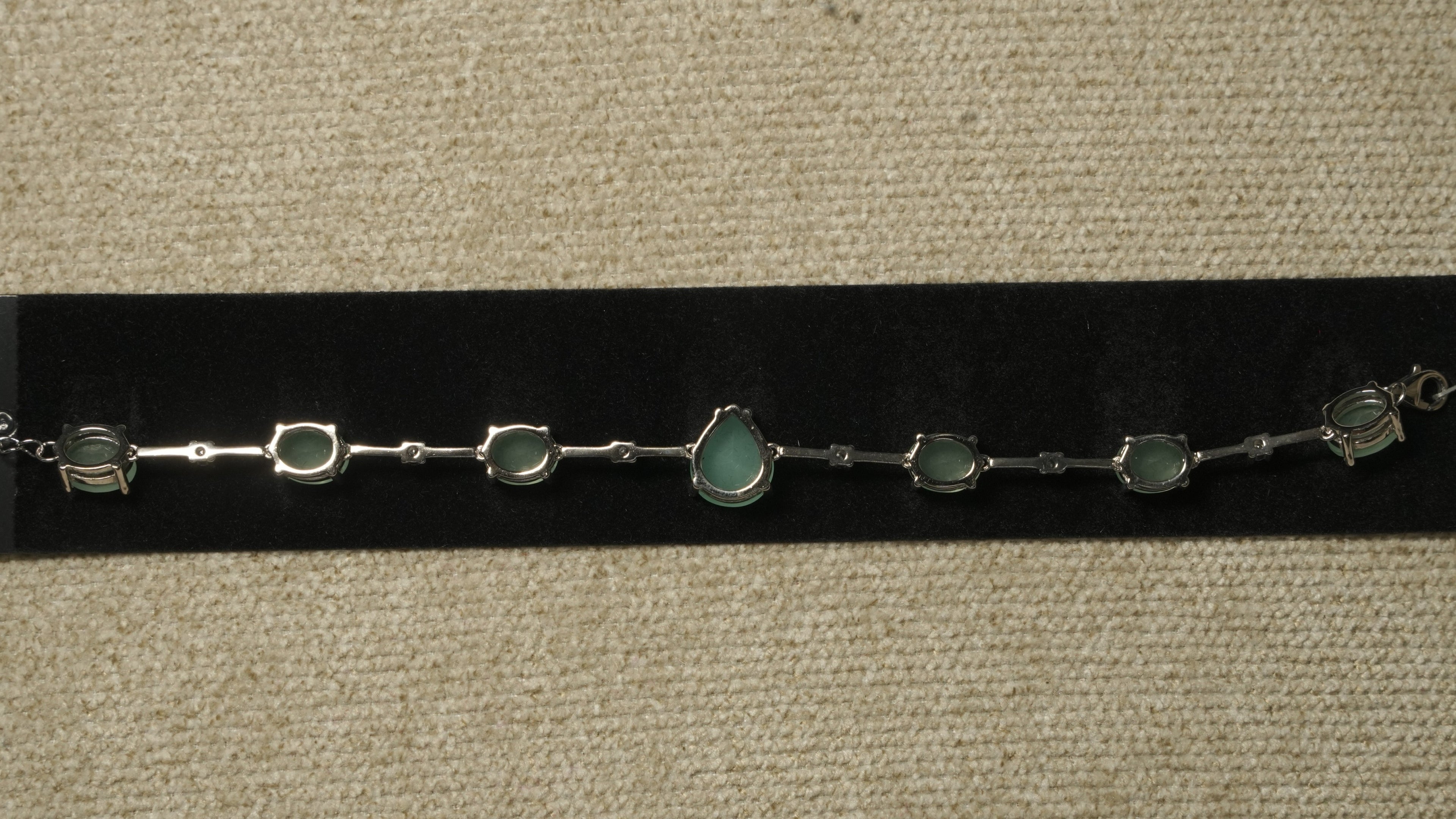 Reverse of the green stone bracelet showing its prong settings, slim bar links and lobster clasp on black velvet.