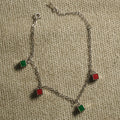 Fine sterling silver cable chain bracelet with alternating red and green enamel square charms and a spring-ring clasp, on beige fabric.