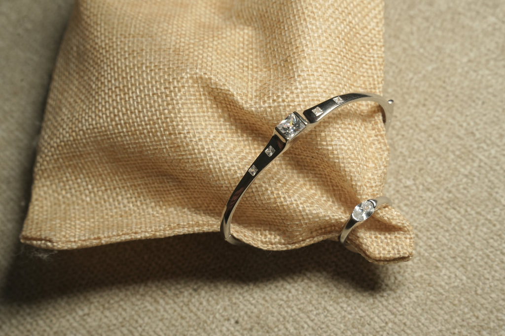 Fine sterling silver kada style bracelet with equal distant square cut stones moving towards the large central squre stone on beige fabric, show together with a Ring of same style