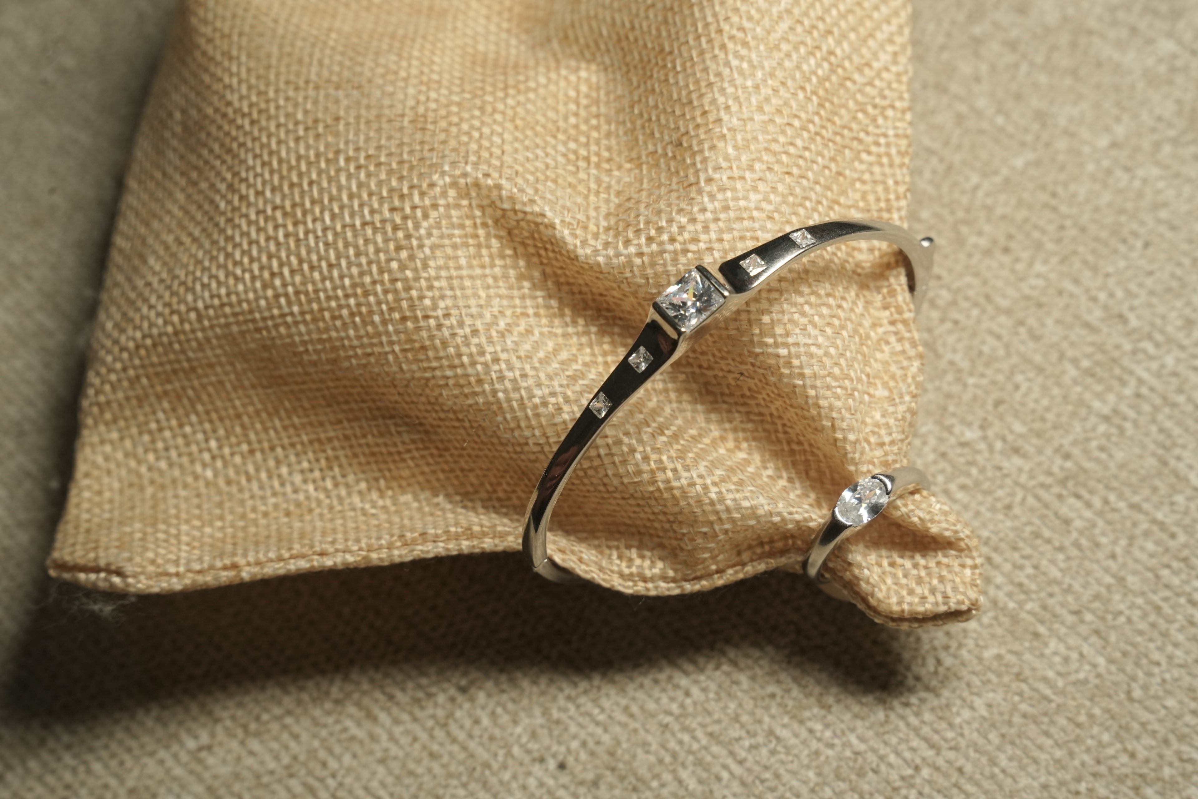 Fine sterling silver kada style bracelet with equal distant square cut stones moving towards the large central squre stone on beige fabric, show together with a Ring of same style