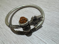 Oxidised sterling silver kada with a trishul, damroo and rudraksha bead, lying on a pale wood surface.