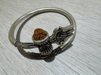 Oxidised sterling silver kada with a trishul, damroo and rudraksha bead, lying on a pale wood surface.