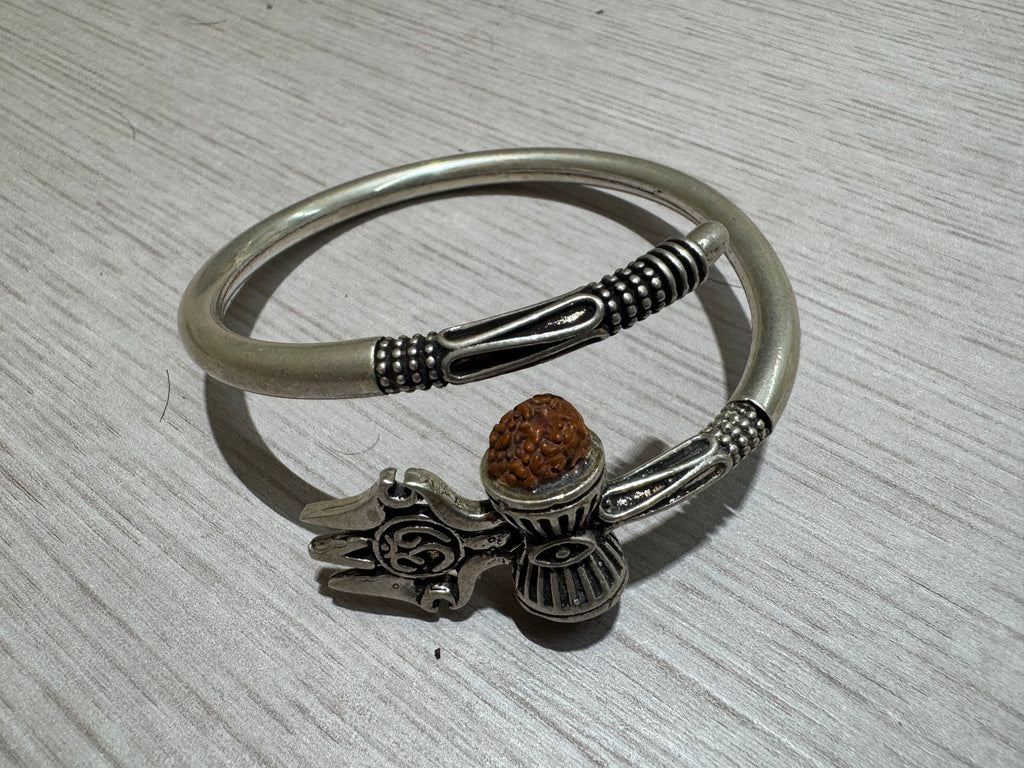 Sterling silver kada seen from above on pale wood, showing the satin band and the granulated collars at both open ends.