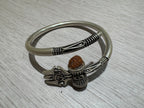 Sterling silver kada seen from above on pale wood, showing the satin band and the granulated collars at both open ends.