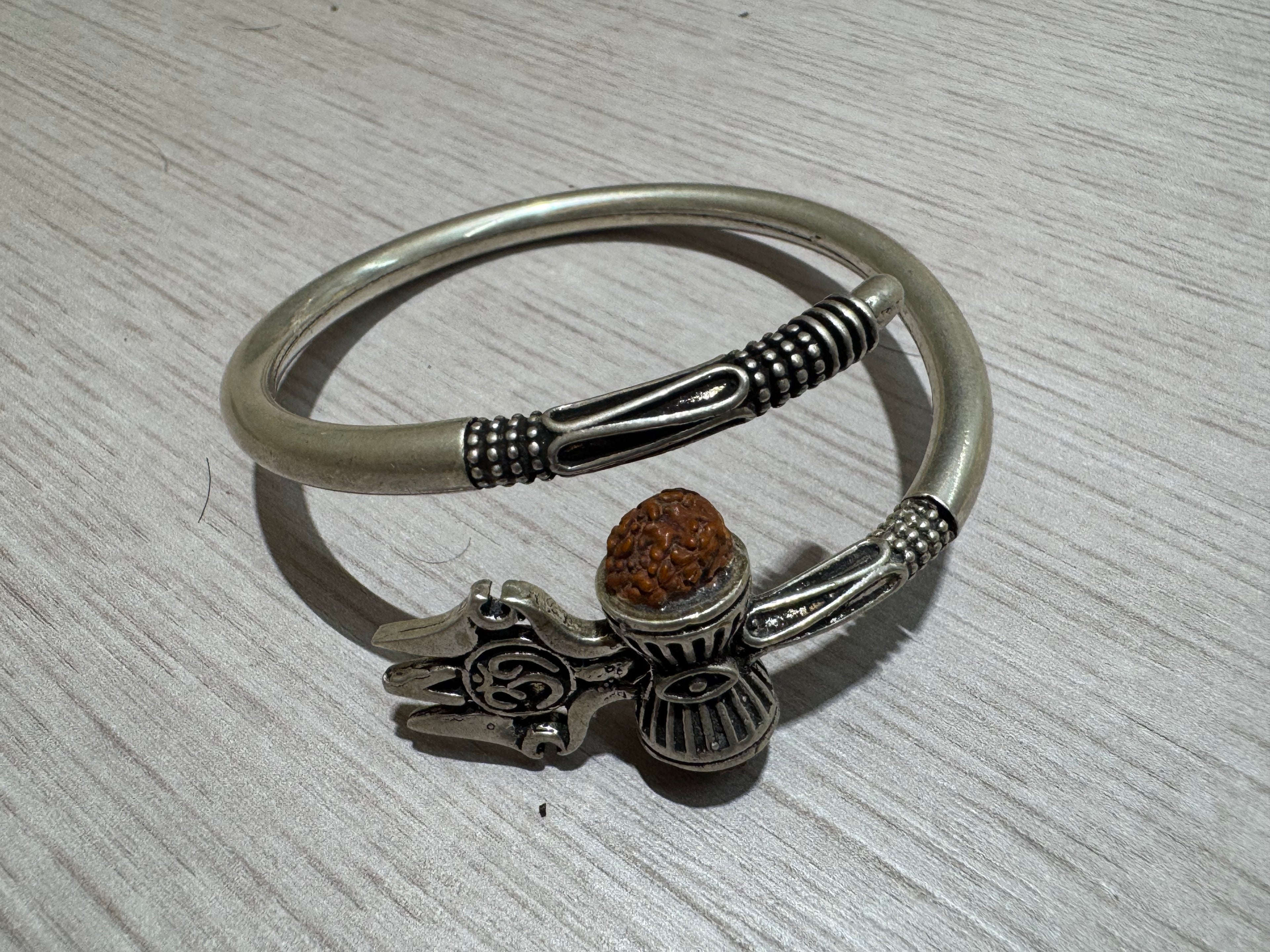 Sterling silver kada seen from above on pale wood, showing the satin band and the granulated collars at both open ends.