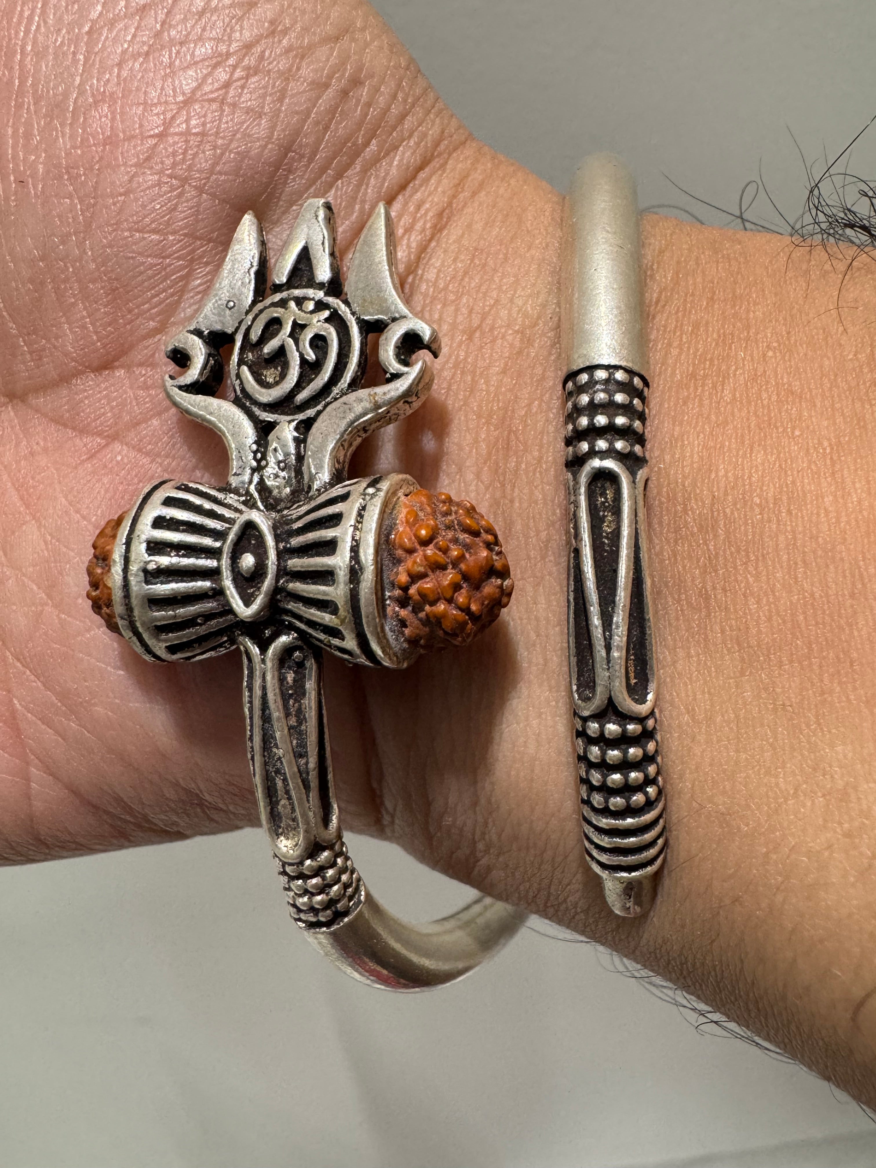 Close view on the wrist of the trishul, the ribbed damroo and the two rudraksha beads on the sterling silver kada.