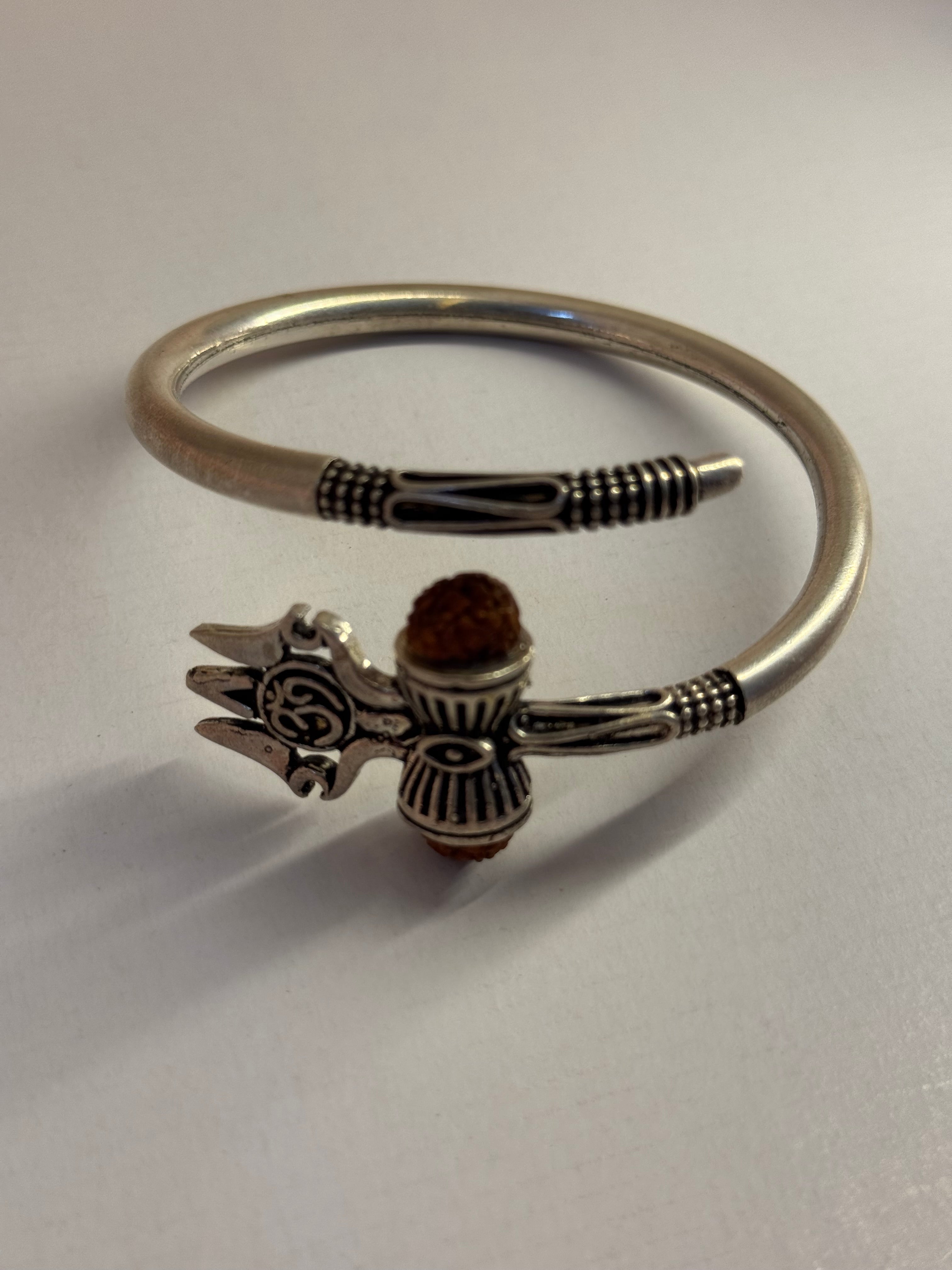 Sterling silver kada laid flat, showing the openwork tapers and the trishul with its carved Om beneath the damroo.