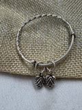Twisted sterling silver bangle on jute cloth, with two oxidised leaf drops hanging at the opening.