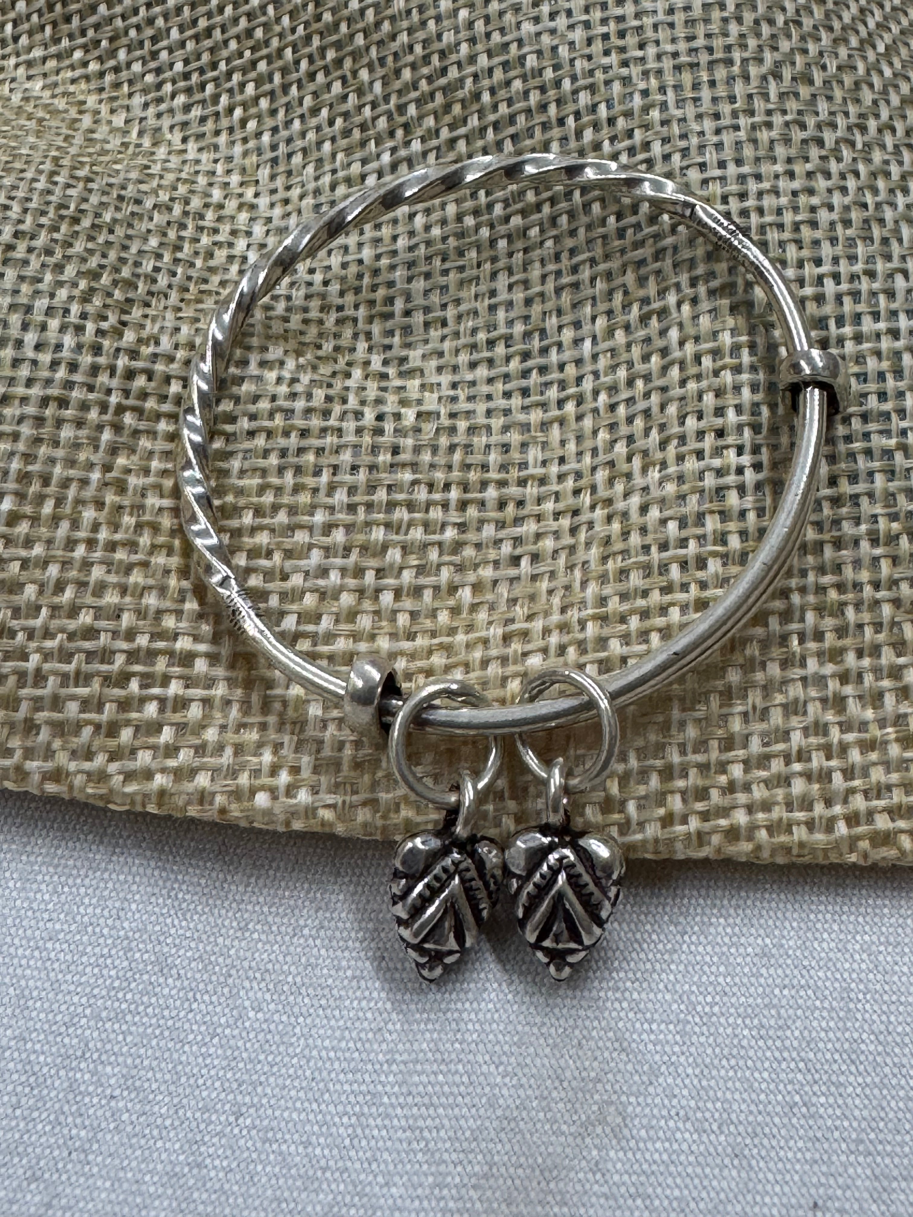 Twisted sterling silver bangle on jute cloth, with two oxidised leaf drops hanging at the opening.
