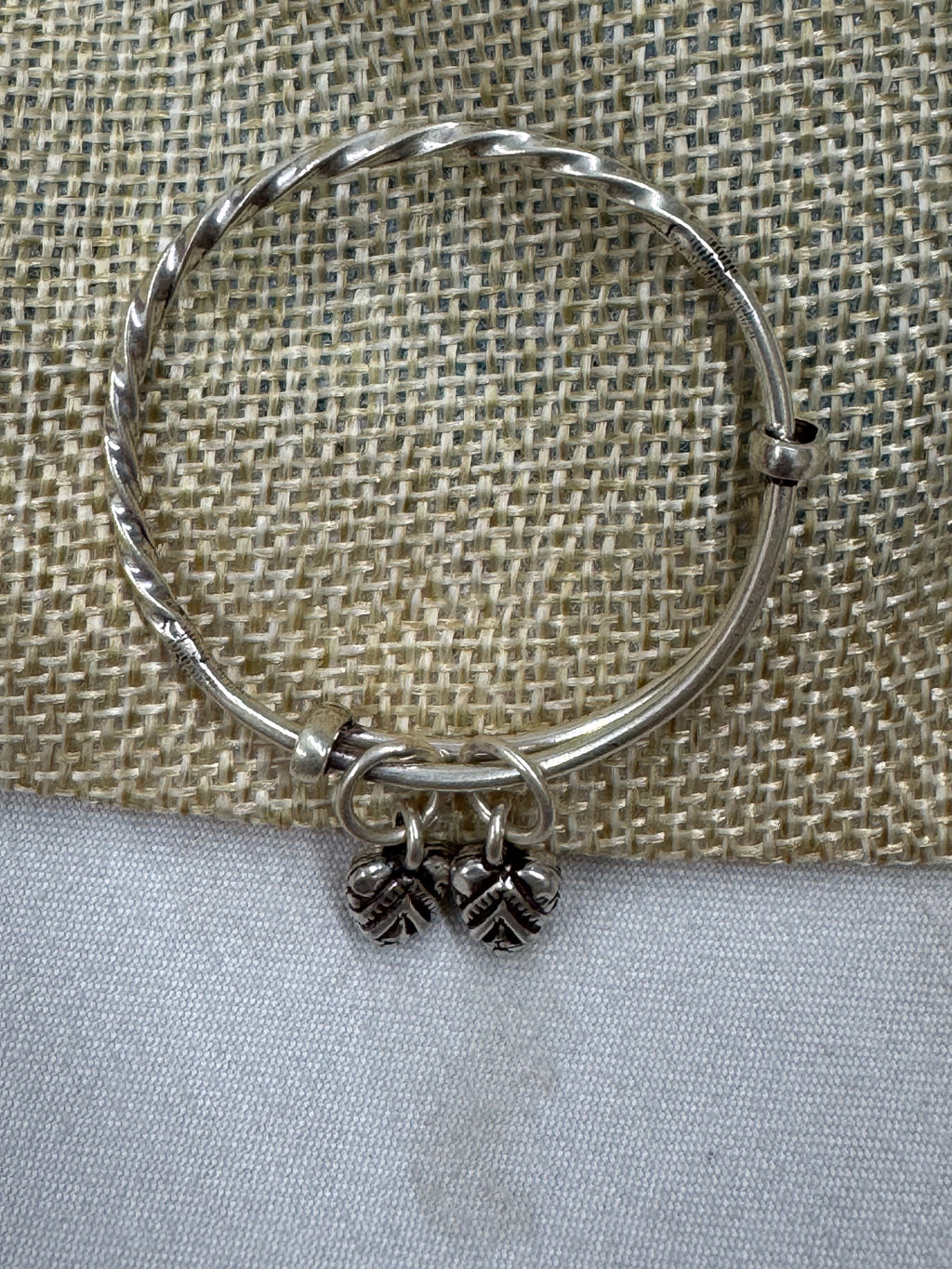 Sterling silver adjustable bangle laid flat across jute and cream cloth, showing the rope twist along the band.