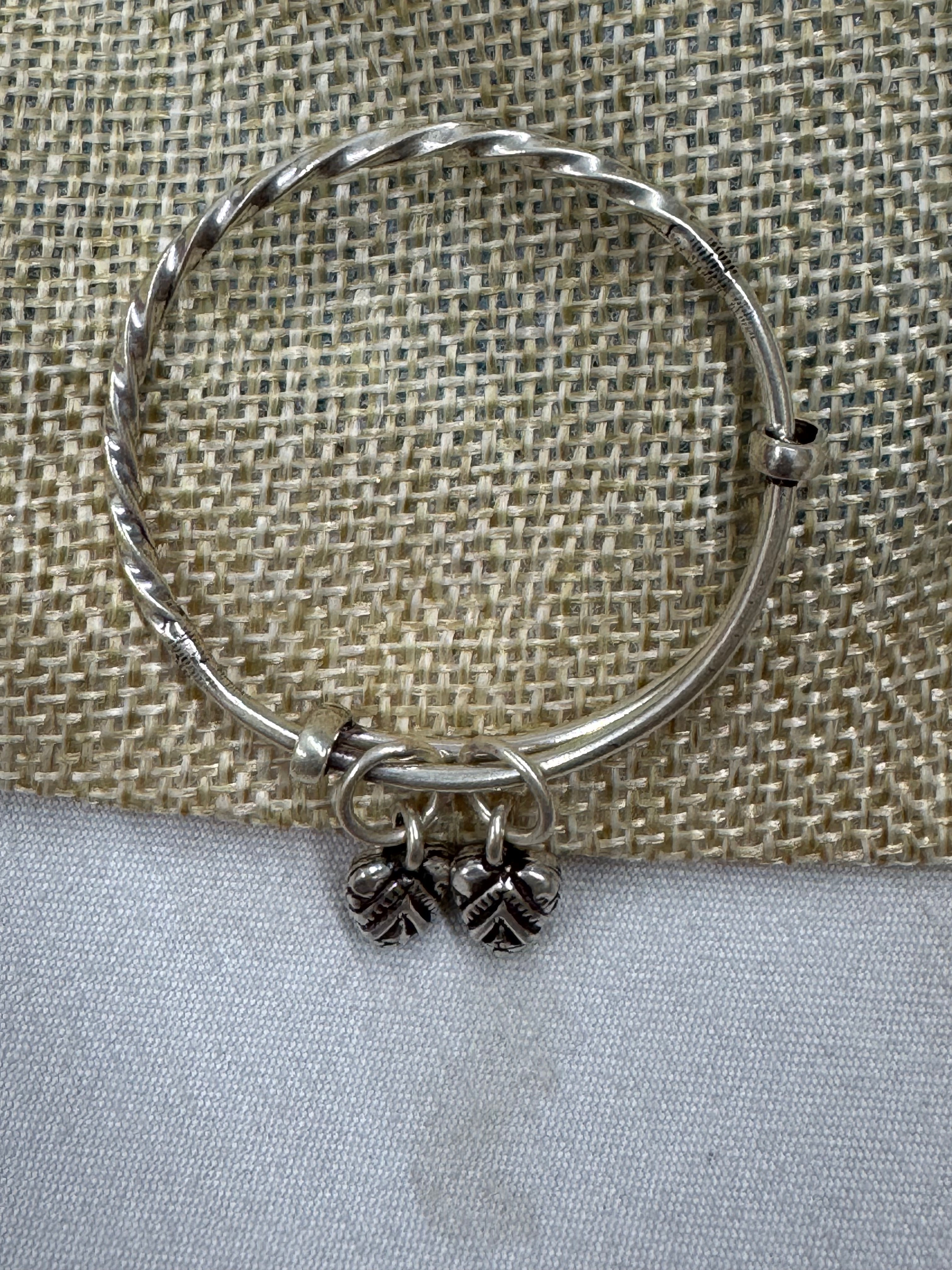 Sterling silver adjustable bangle laid flat across jute and cream cloth, showing the rope twist along the band.