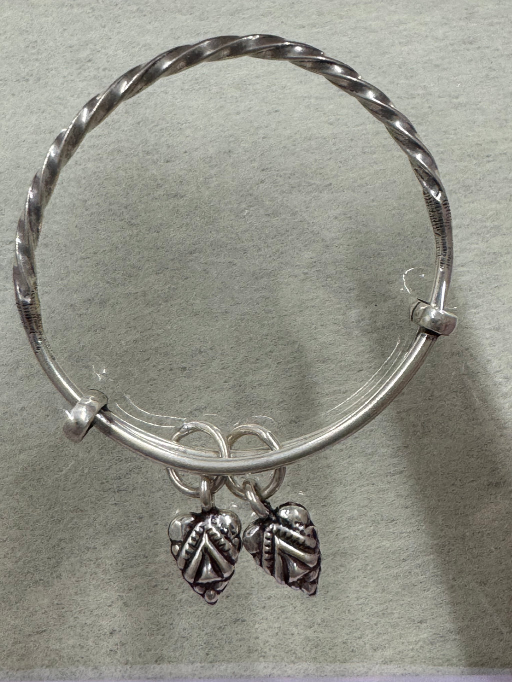 Overhead view of the twisted sterling silver bangle on a pale grey ground, both leaf drops to one side.