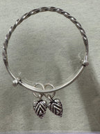 Overhead view of the twisted sterling silver bangle on a pale grey ground, both leaf drops to one side.
