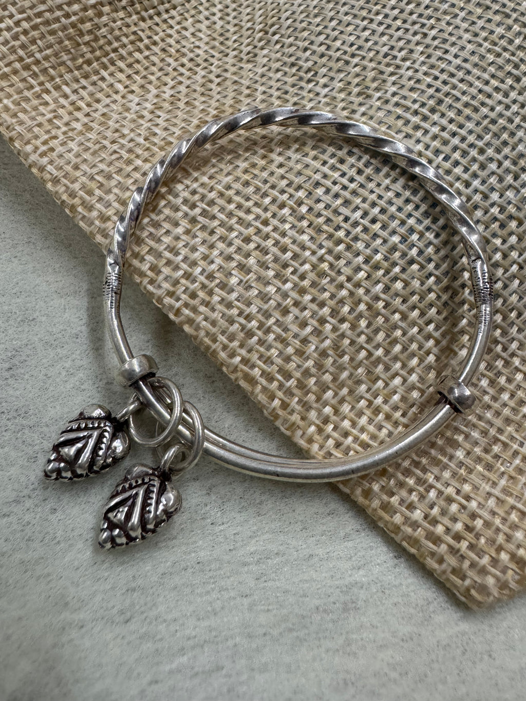 Sterling silver bangle resting against jute with the leaf drops gathered at the front of the opening.